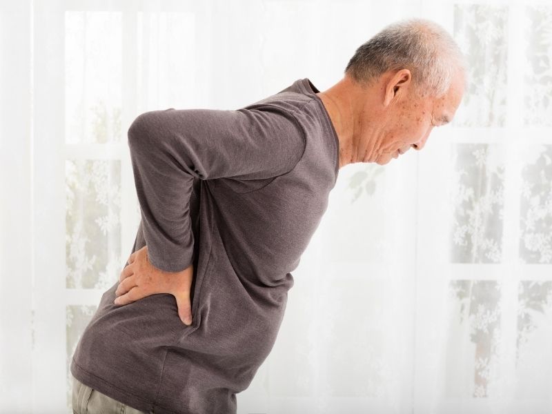 elderly man with his hands on lower back in pain