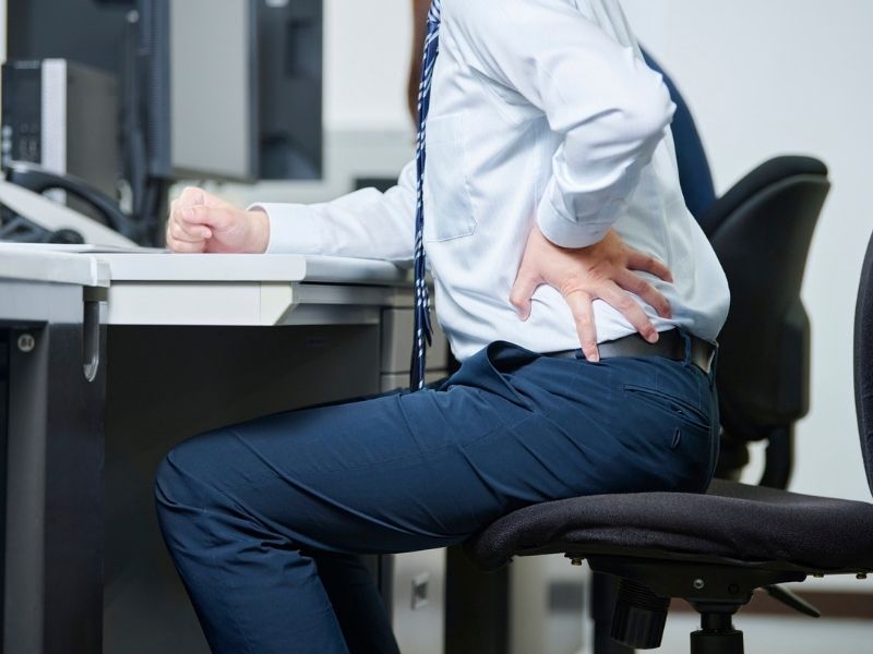 man sitting at desk holding his lower back and hip in pain