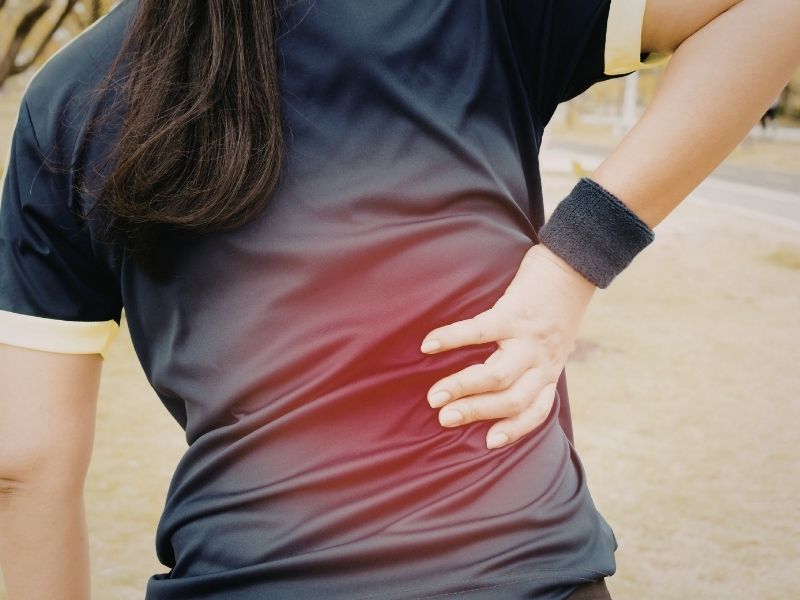 woman exercising on a run, with her hand on her lower back in pain