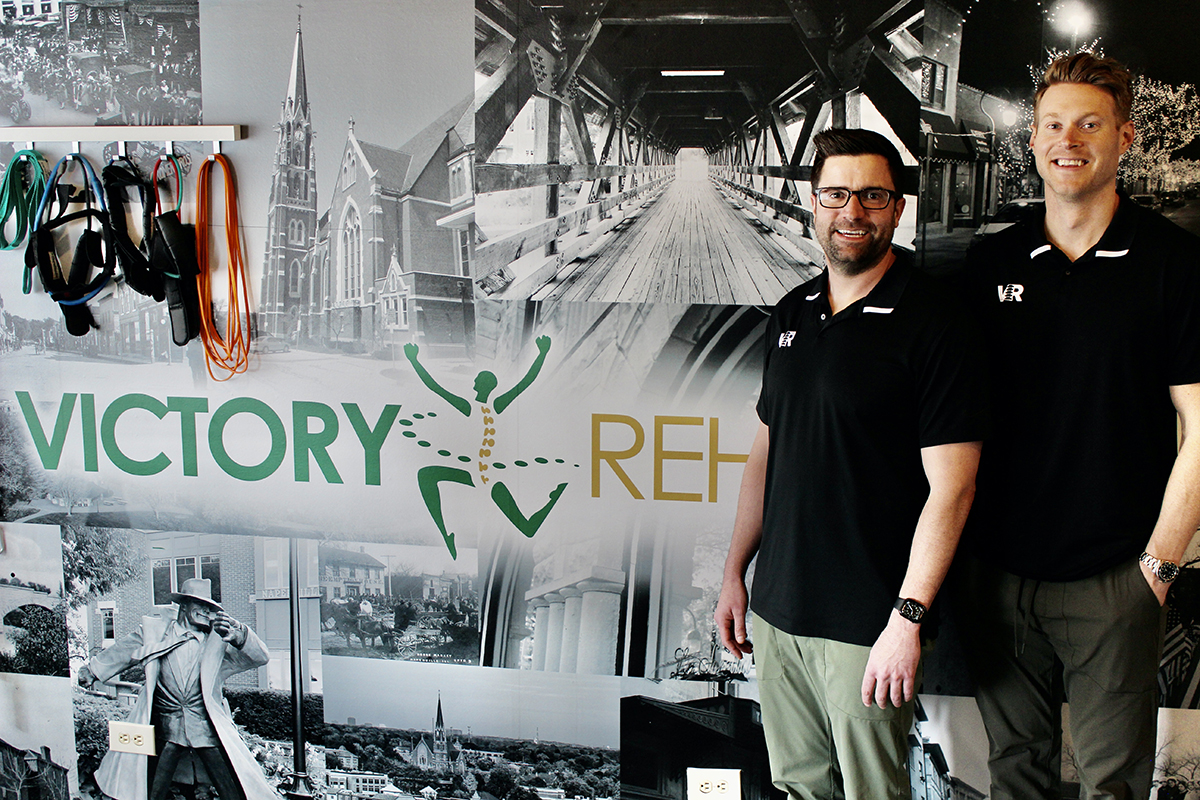 Dr. Chris and Dr. Tom with Victory Rehab Chiropractic logo on wall